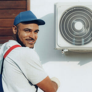 A smiling man works on an air conditioner in this image.