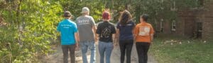 Image showing the backs of five members of Avivo's street outreach team as they walk through an alley. They're all wearing different Avivo shirts.
