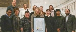 Group of Avivo staff, an Avivo program participant, Wildflyer Coffee staff, and City of Minneapolis staff pose for a photo at Minneapolis City Hall.