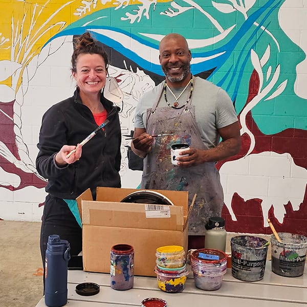 Photo of two artists taking a break and posing while helping paint a mural at Avivo Village.