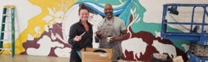 Photo of two artists taking a break and posing while helping paint a mural at Avivo Village.