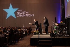 Image from Avivo Night of Champions event showing two men standing on stage, addressing the audience.